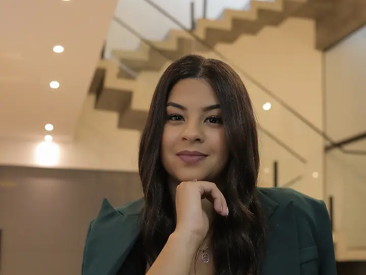 Dra. Akemy Rande de Sousa, de blazer verde, sentada à mesa, com a mão no queixo
